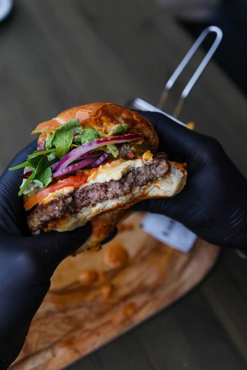 Black Angus burger doorgesneden in zwarte handschoen, met rode ui en rucola