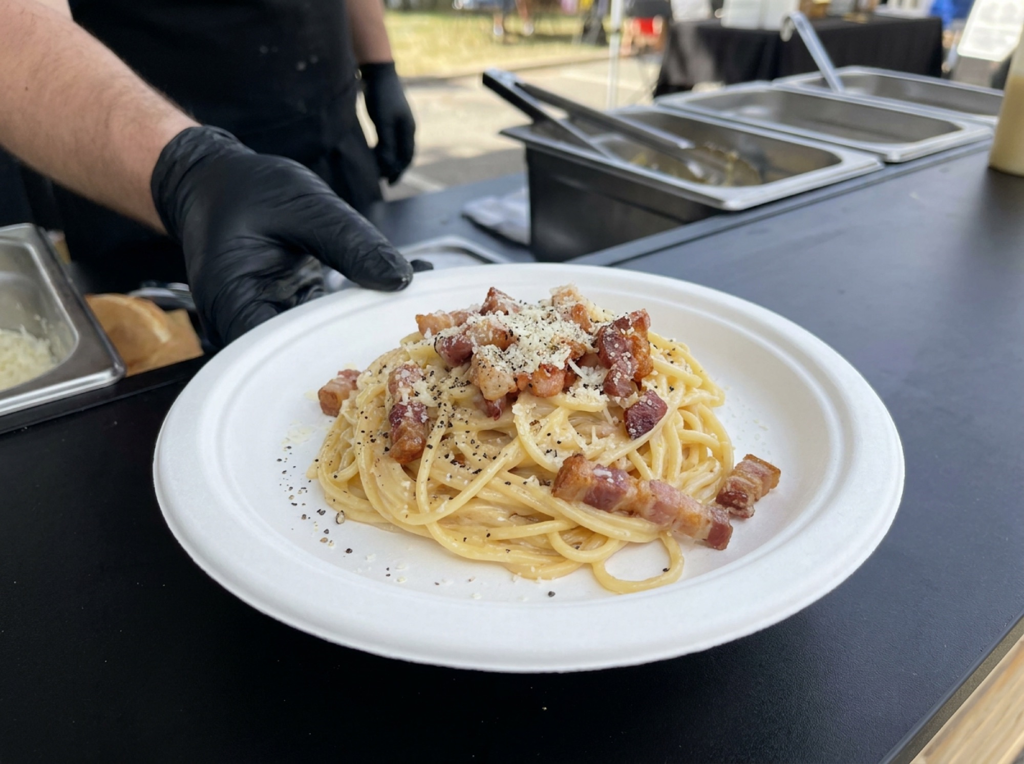 Pasta carbonara op wit suikerrietbord aan de cateringcounter, afgewerkt met spek en zwarte peper