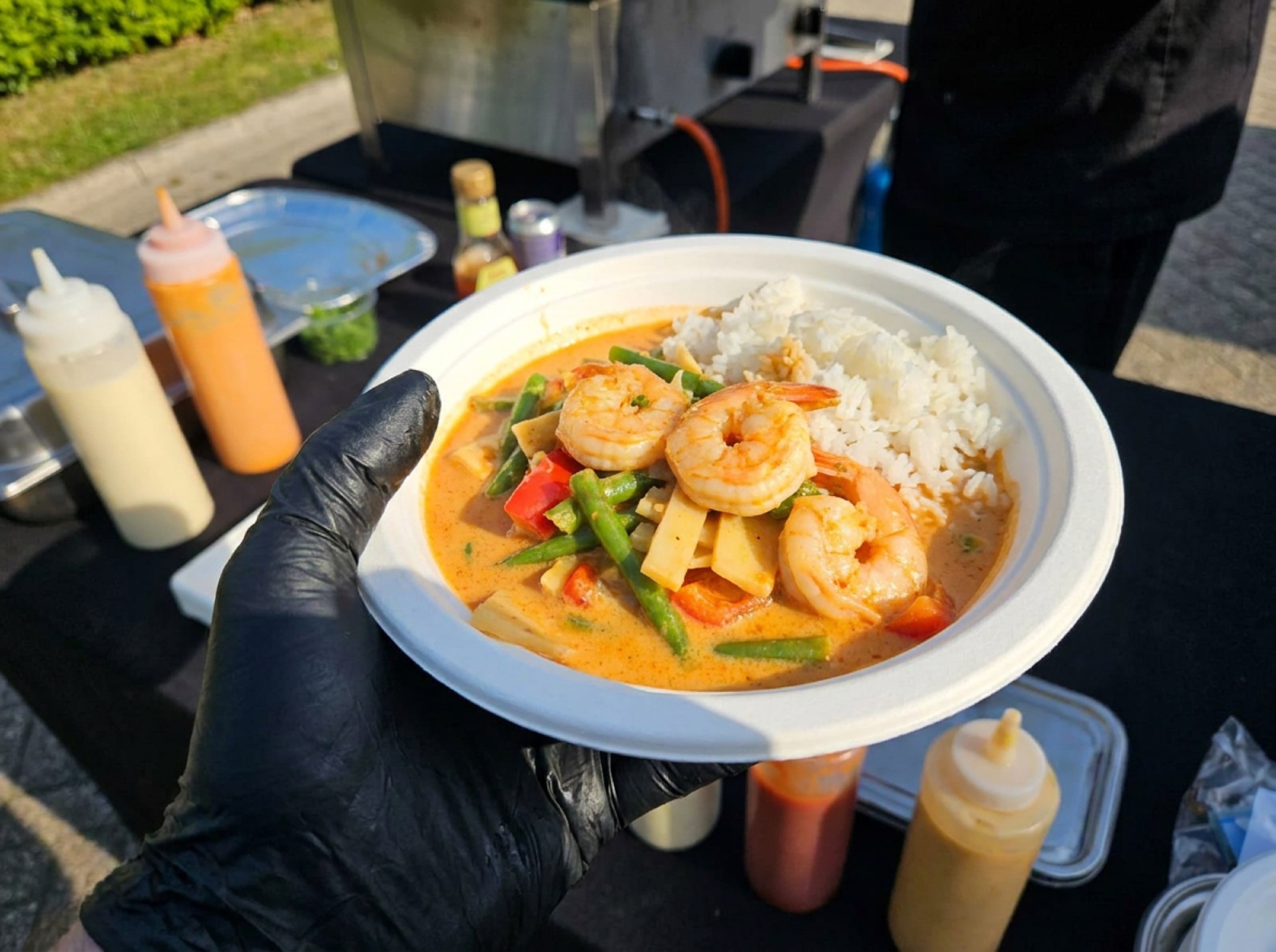 Thaise curry met scampi, groenten en rijst in wit suikerrietbord, geserveerd met zwarte handschoenen